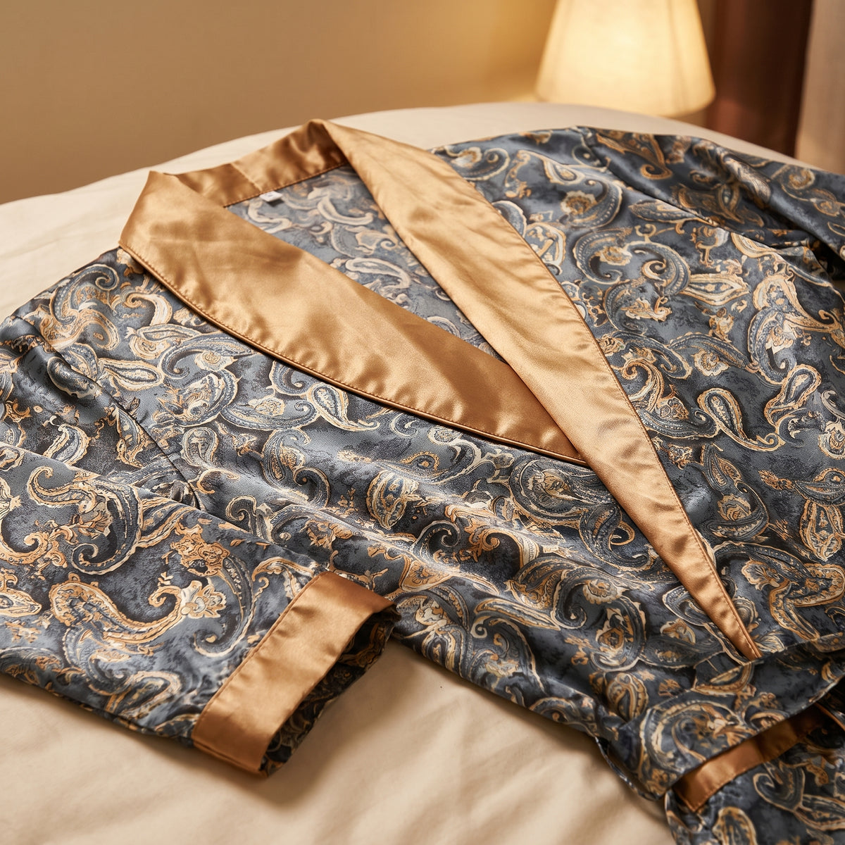Gros plan du col châle en satin doré uni d’une robe de chambre grise à motif paisley, sa couture et le poignet doré