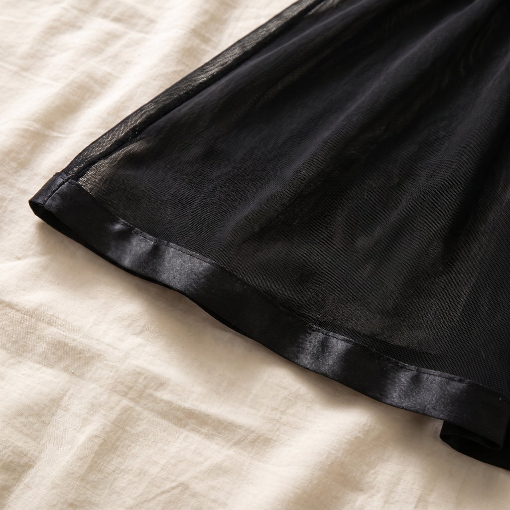 Bas de la jupe vu de près, biais de satin noir ourlant le voile transparent
