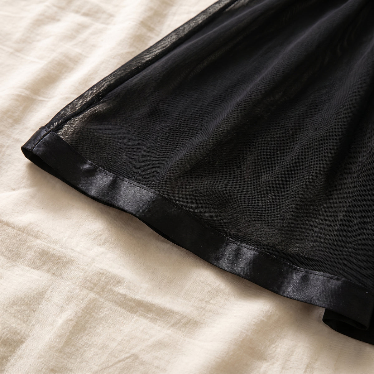 Bas de la jupe vu de près, biais de satin noir ourlant le voile transparent