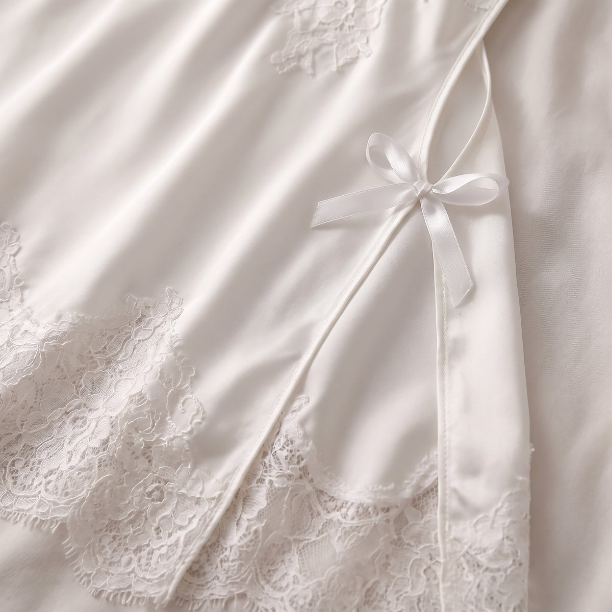 Détail de l'ourlet en dentelle blanche et de la fente fermée par un noeud satin