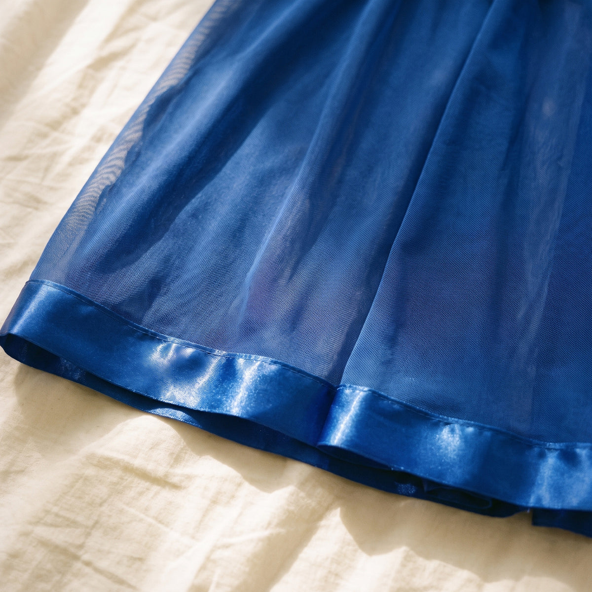 Bas de la jupe vu de près, large biais de satin brillant ourlant le voile transparent
