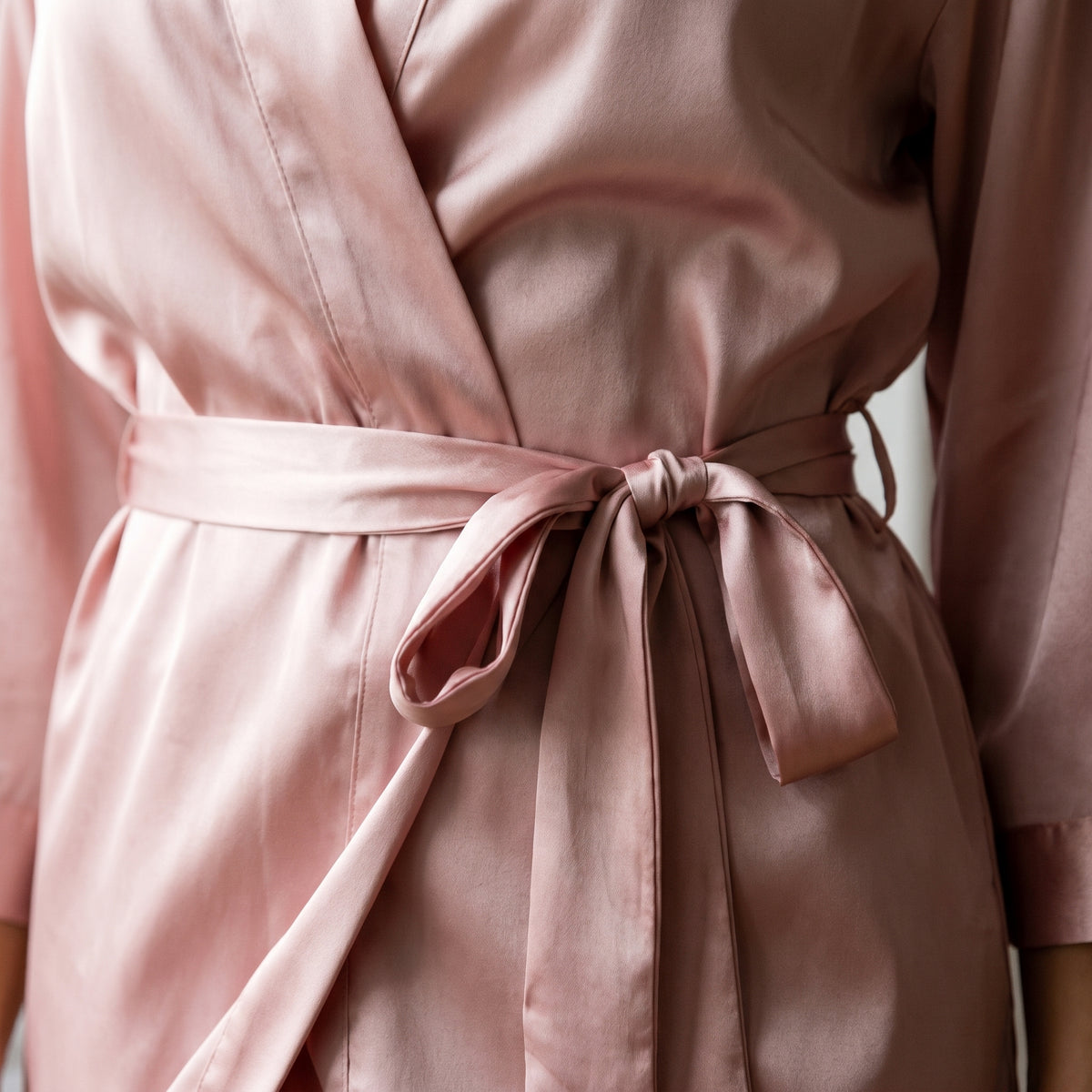 Nœud de la ceinture du peignoir satiné rose vu de près, et son passant de tissu