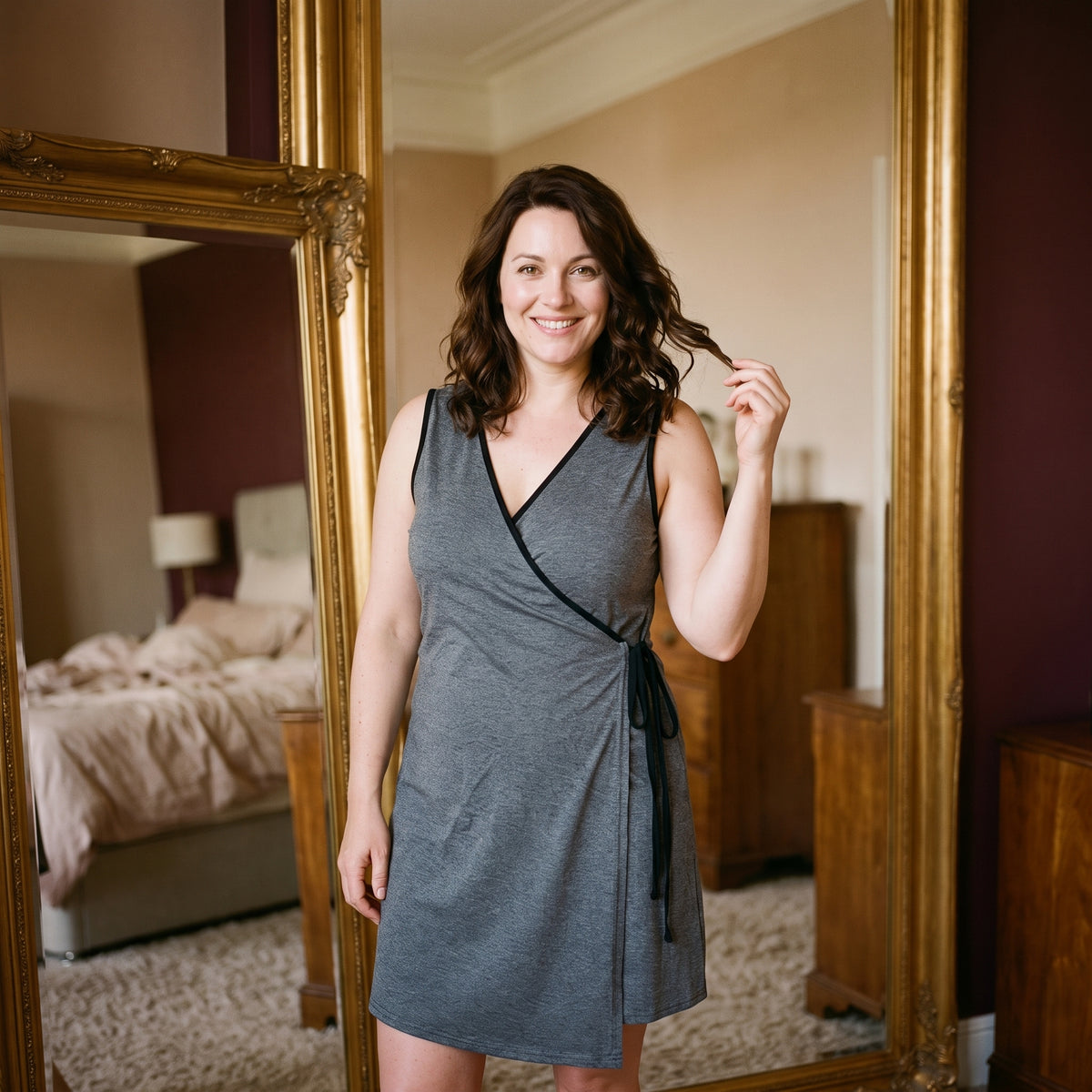 Femme souriante devant le miroir de sa chambre, le soir, dans la nuisette d’allaitement grise