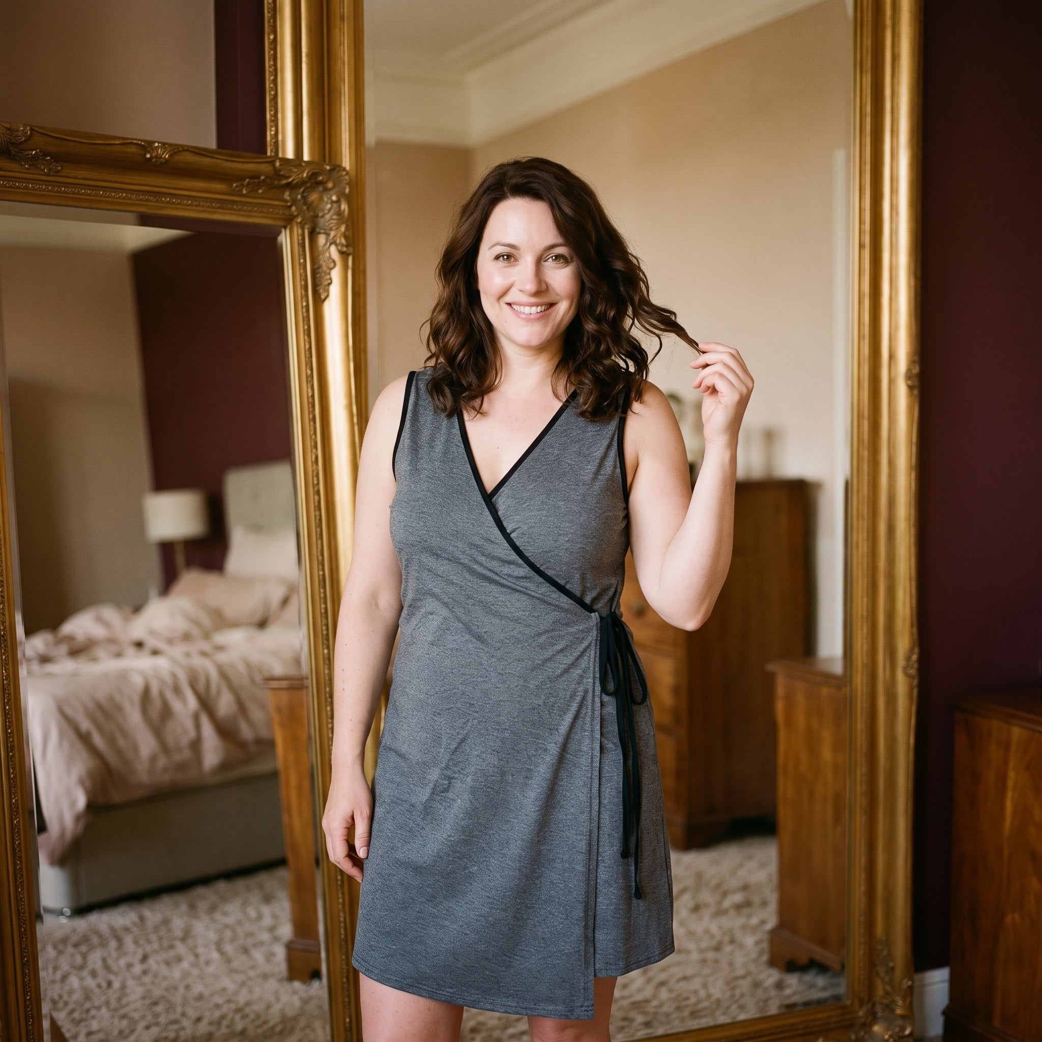 Femme souriante devant le miroir de sa chambre, le soir, dans la nuisette d’allaitement grise Image