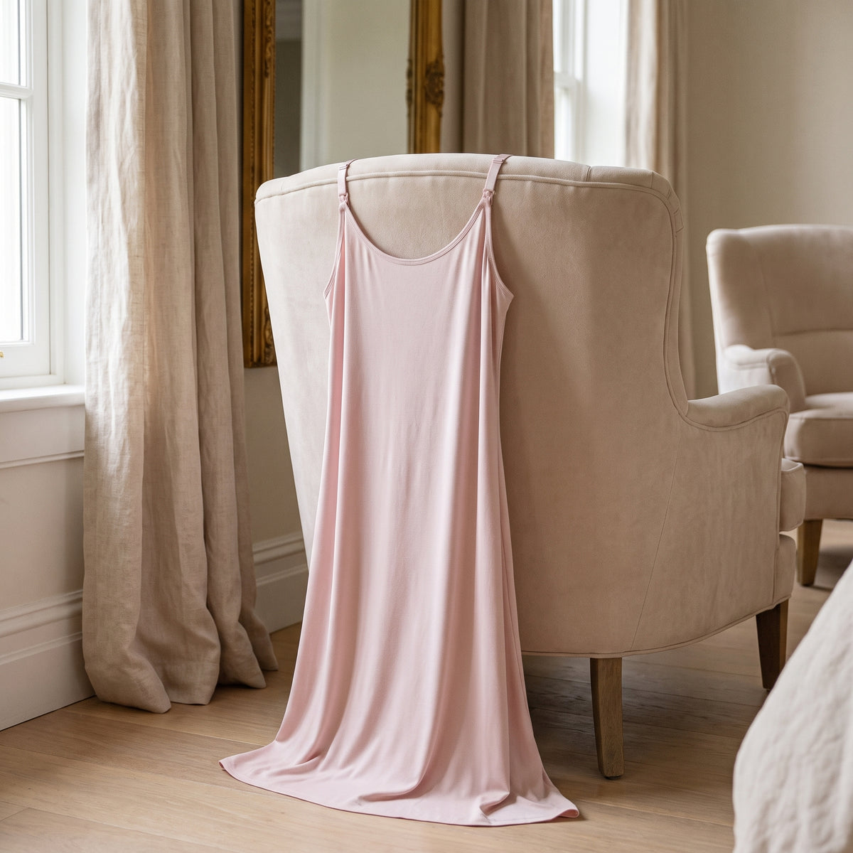 Nuisette d’allaitement rose posée sur un fauteuil de boudoir, la douceur du rose poudré et le tombé souple du tissu