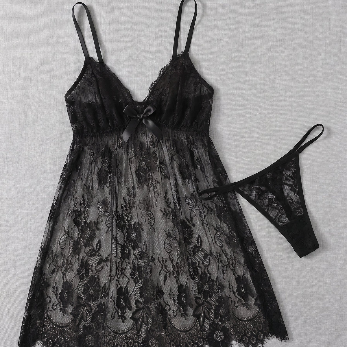 Nuisette babydoll en dentelle noire posée à plat avec son string assorti, ourlet festonné à picots