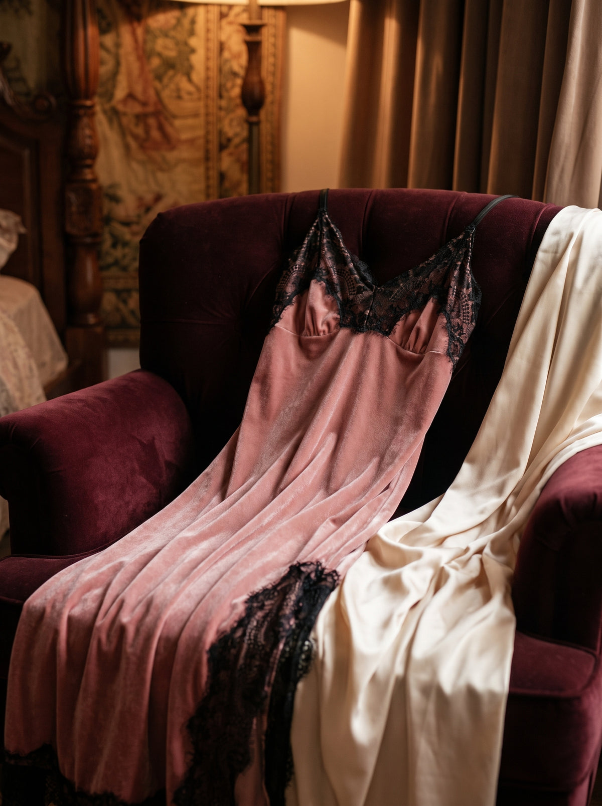 Nuisette longue en velours rose drapée sur un fauteuil boudoir en velours bordeaux, ambiance intime et chaleureuse