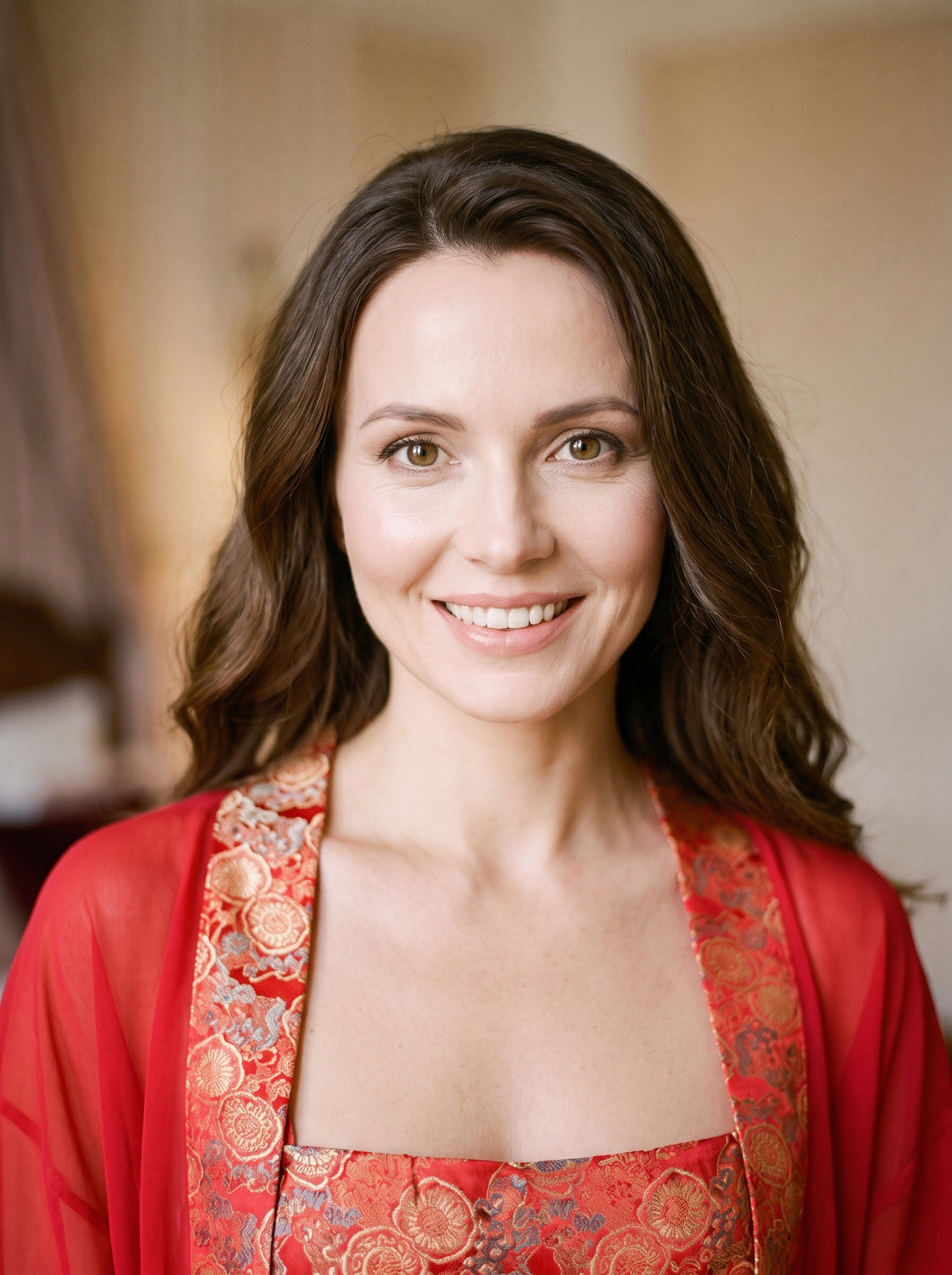 Nuisette string rouge en brocart et voile transparent, modele souriant au visage visible, portant le peignoir assorti, ambiance boudoir