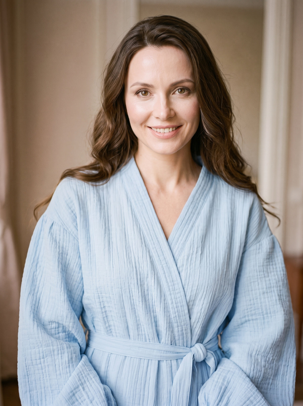 Portrait de la modèle brune portant le peignoir spa bleu ciel en coton gaufré, souriante, décor boudoir