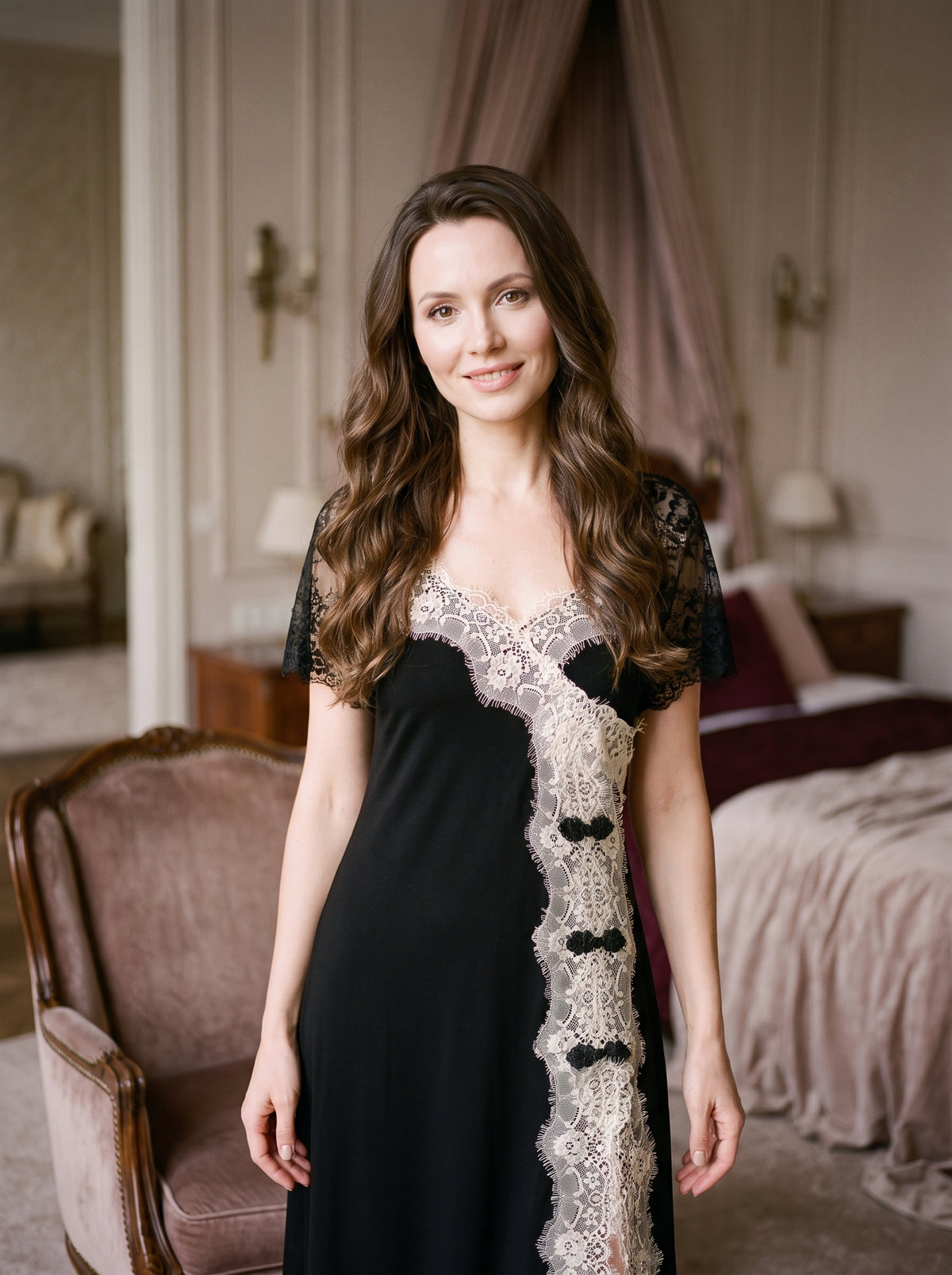 Femme brune souriante portant la chemise de nuit noire en dentelle, regard doux vers l'objectif, fond boudoir tamise, cadrage mi-cuisse
