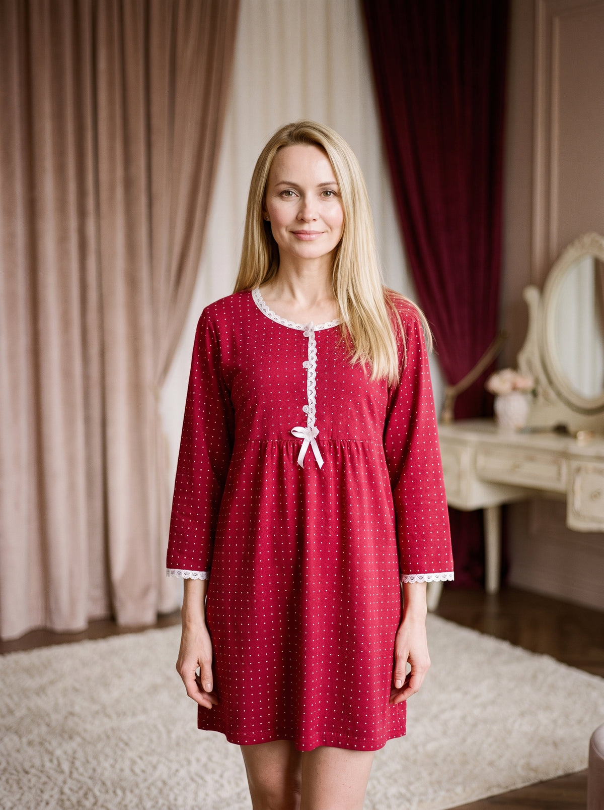 Modele blonde portant la nuisette longue rouge a pois en coton, souriante, dans un boudoir elegant