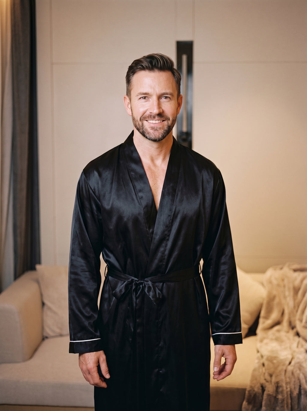 Homme portant la robe de chambre satinee noire, debout, souriant, decor boudoir