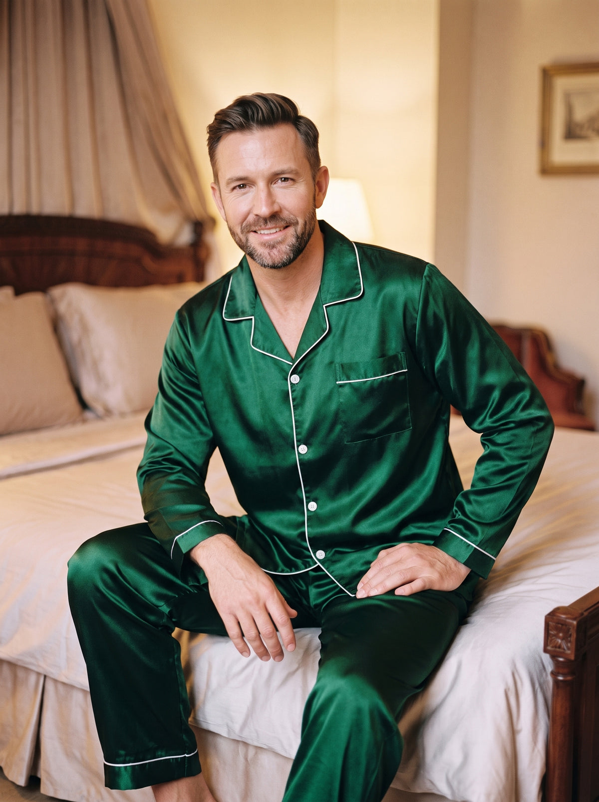 Pyjama homme en satin vert émeraude porté assis au bord du lit, liseré blanc à l'ourlet du pantalon