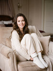 Femme souriante assise dans un fauteuil boudoir portant des chaussettes blanches cocooning, intérieur polaire moelleux visible
