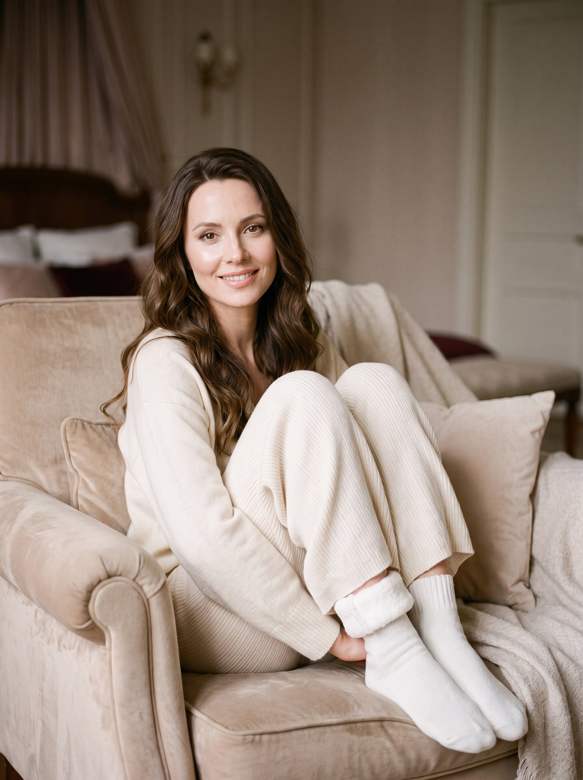 Femme souriante assise dans un fauteuil boudoir portant des chaussettes blanches cocooning, intérieur polaire moelleux visible