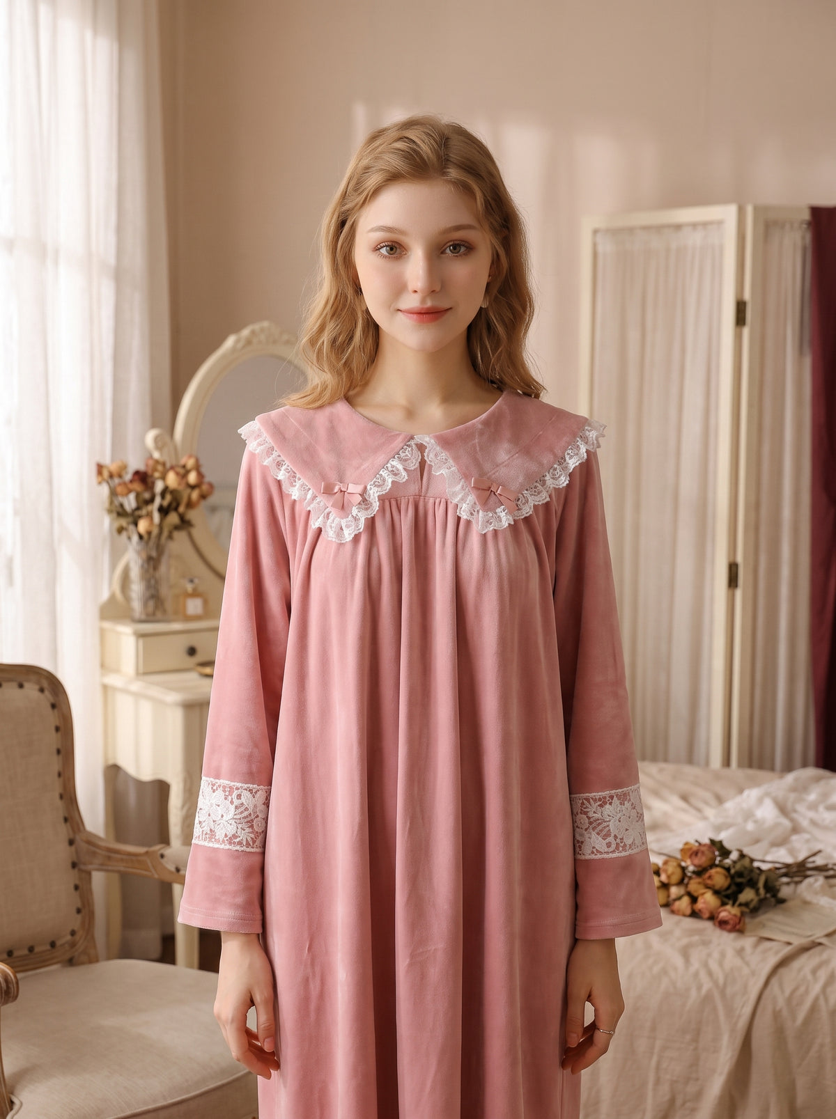 Modele souriante portant la robe de nuit princesse en velours rose, col Claudine en dentelle blanche, cadrage mi-cuisse dans un decor boudoir