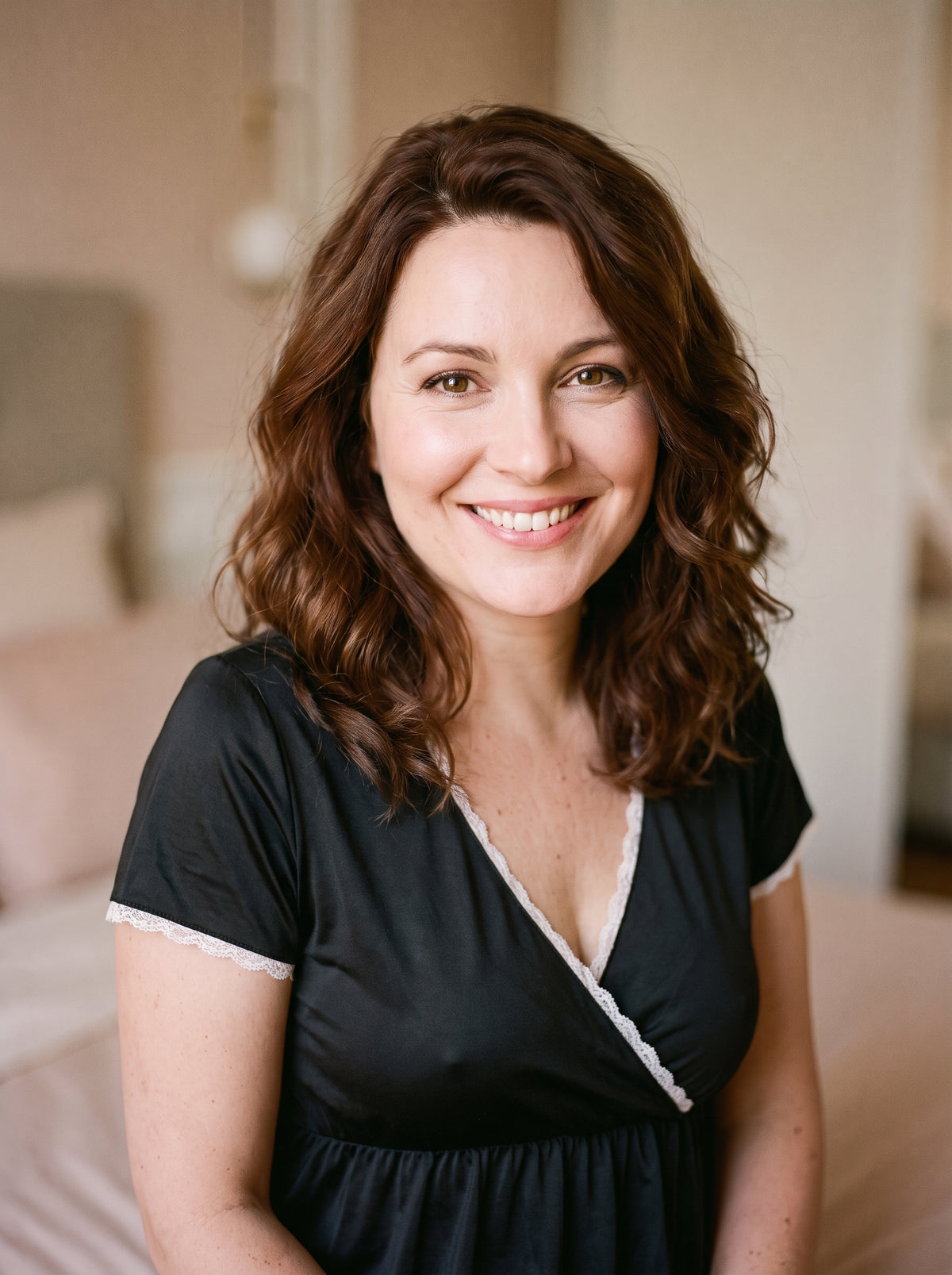 Femme enceinte souriante portant la nuisette de maternité noire cache-cœur à dentelle blanche, décor boudoir