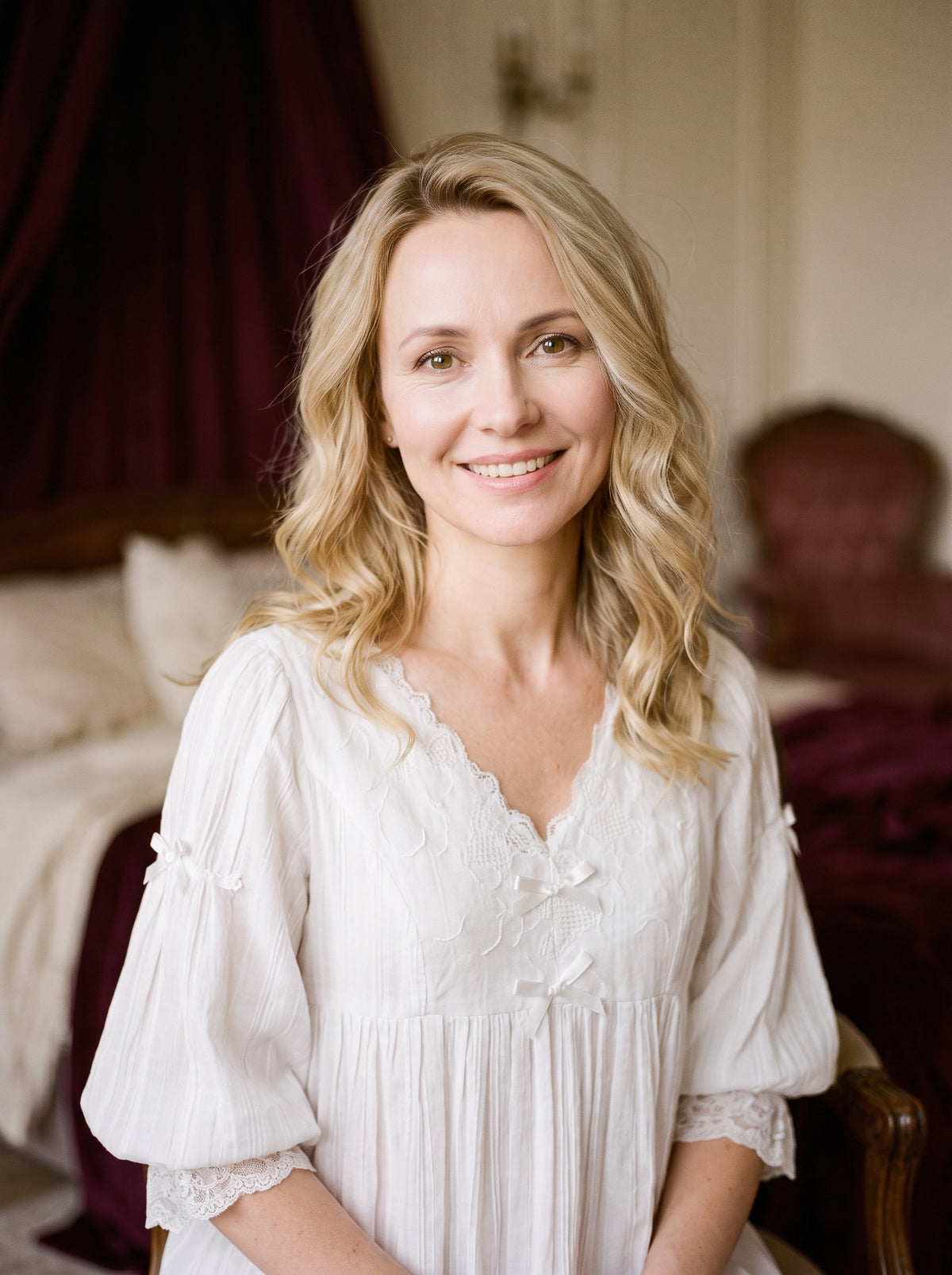 Nuisette blanche vintage à nœuds portée par une femme souriante dans un boudoir aux tons crème et bordeaux