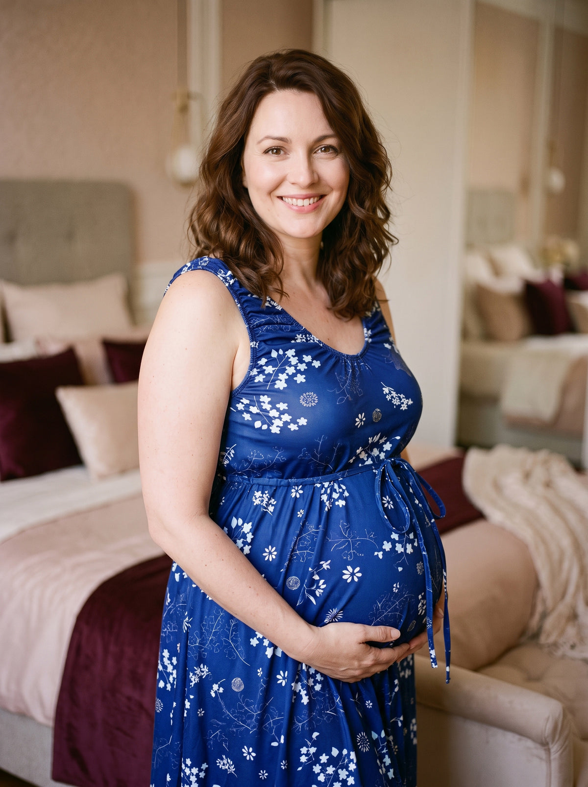 Future maman souriante en nuisette de maternité bleue à fleurs blanches, cordon noué sous la poitrine