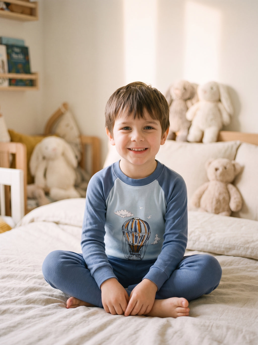 Enfant portant le pyjama garcon en coton a motif montgolfieres, assis sur son lit