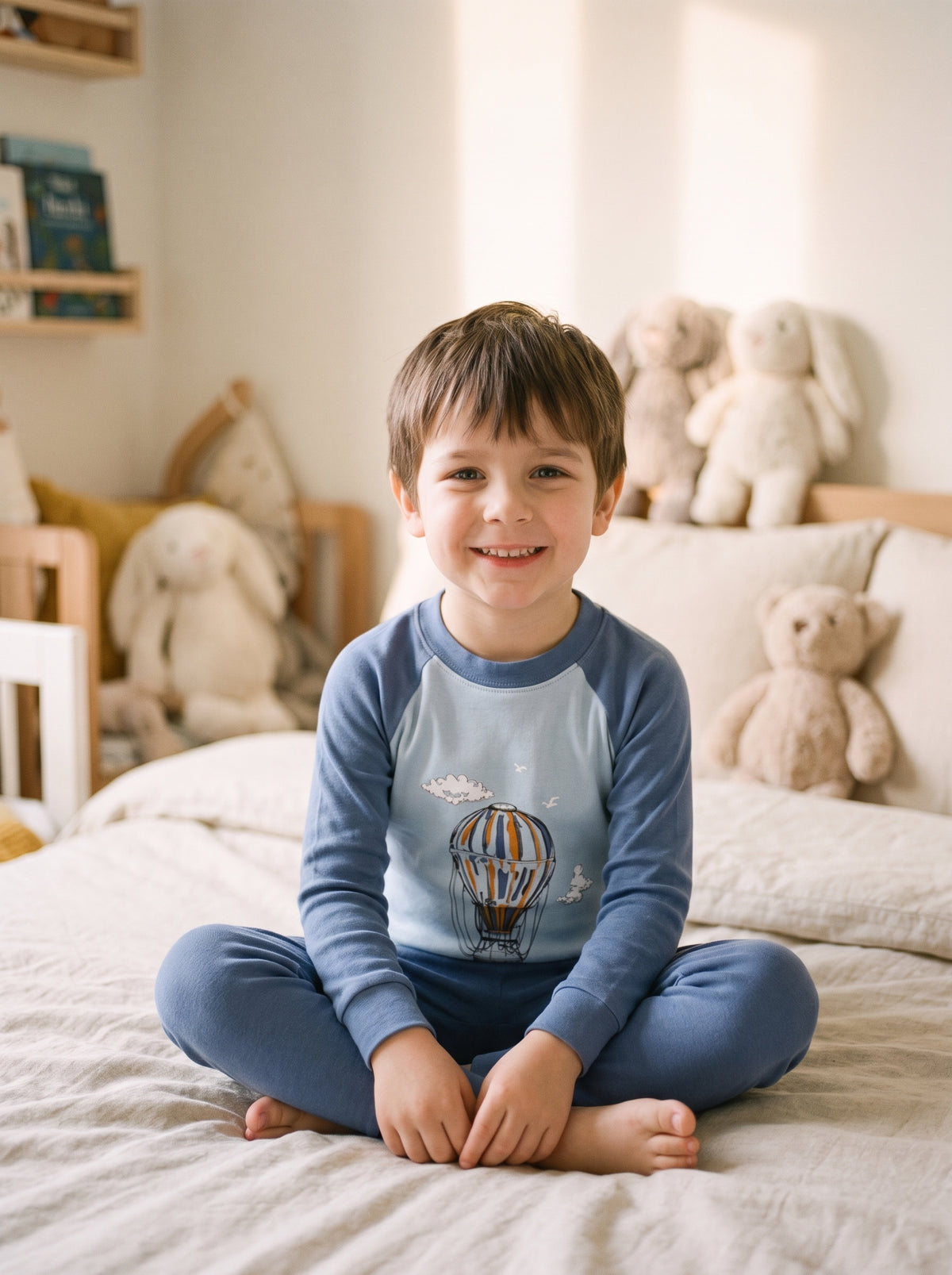 Enfant portant le pyjama garcon en coton a motif montgolfieres, assis sur son lit