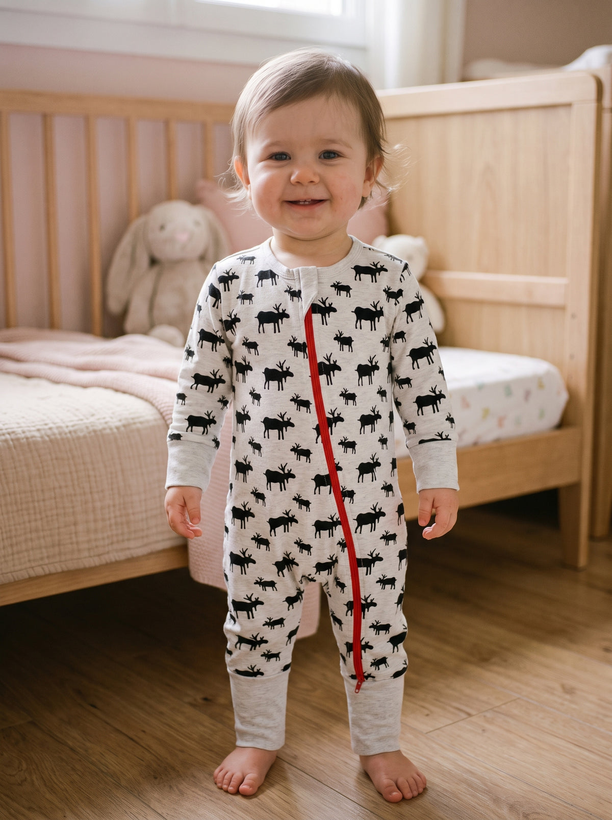 Bébé souriant portant un pyjama gris clair à rennes noirs et fermeture rouge