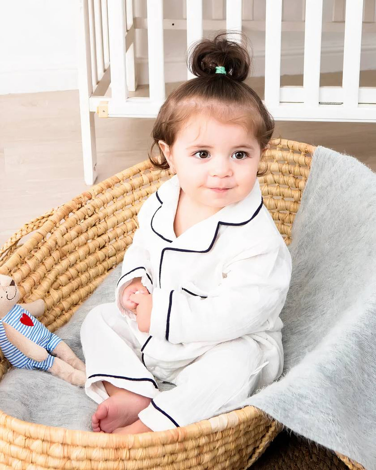 Bébé assis dans un couffin avec le pyjama blanc à col rabattu et liserés noirs