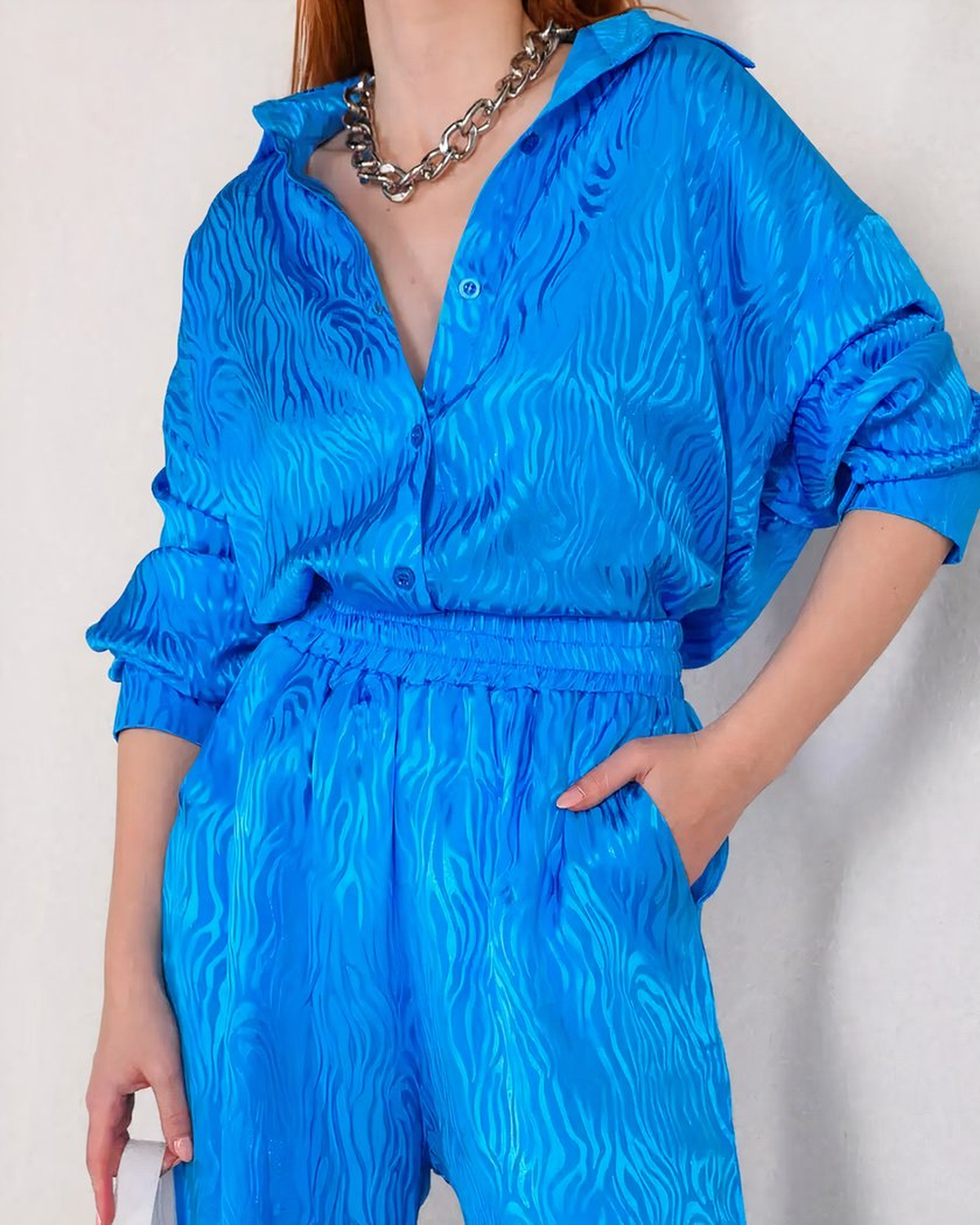 Détail du pyjama bleu satiné : col à deux pointes, patte de boutonnage et taille froncée du pantalon, une main dans la poche