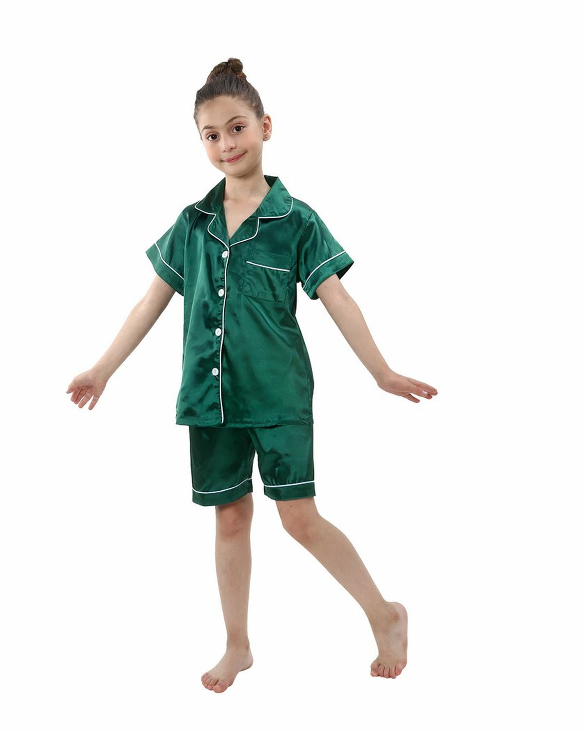 Petite fille souriante debout en pyjama deux pièces vert émeraude satiné, chemise à manches courtes boutonnée et short assorti bordés d'un liseré blanc