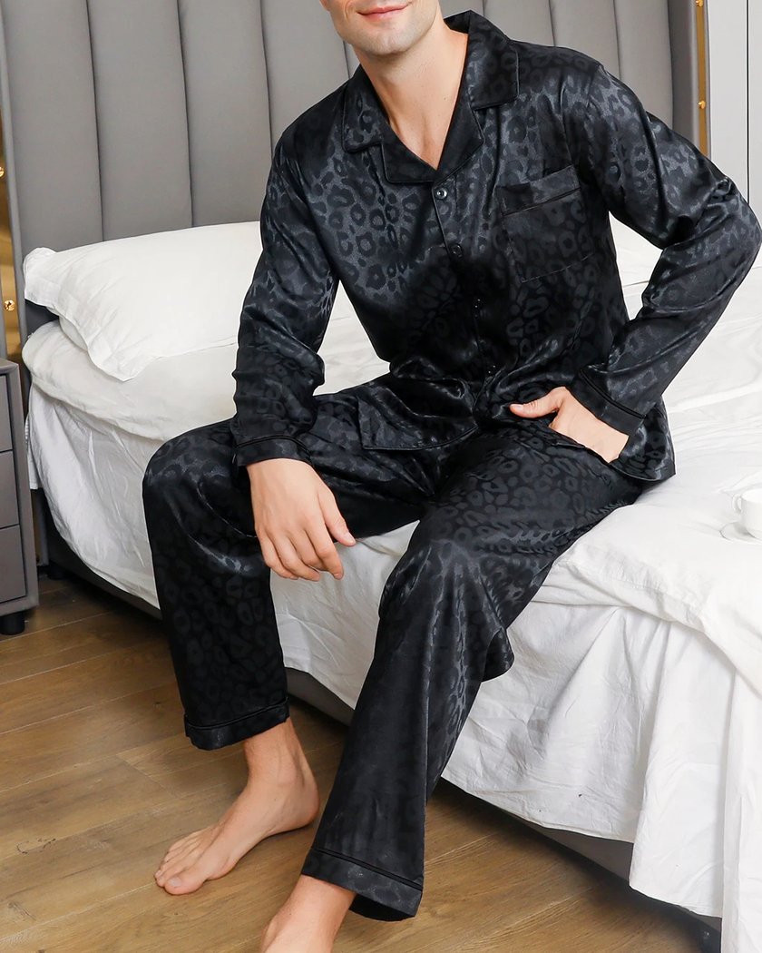 Pyjama homme en satin noir à motif léopard porté assis au bord du lit