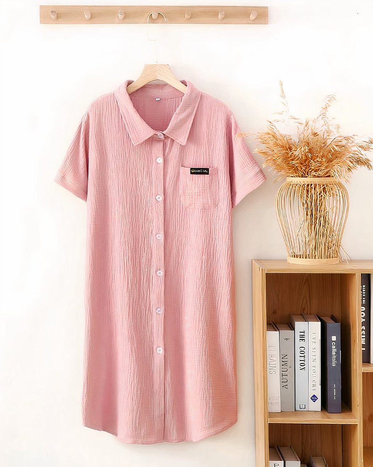 Robe de chambre boutonnée rose suspendue à une patère, poche de poitrine et ourlet arrondi
