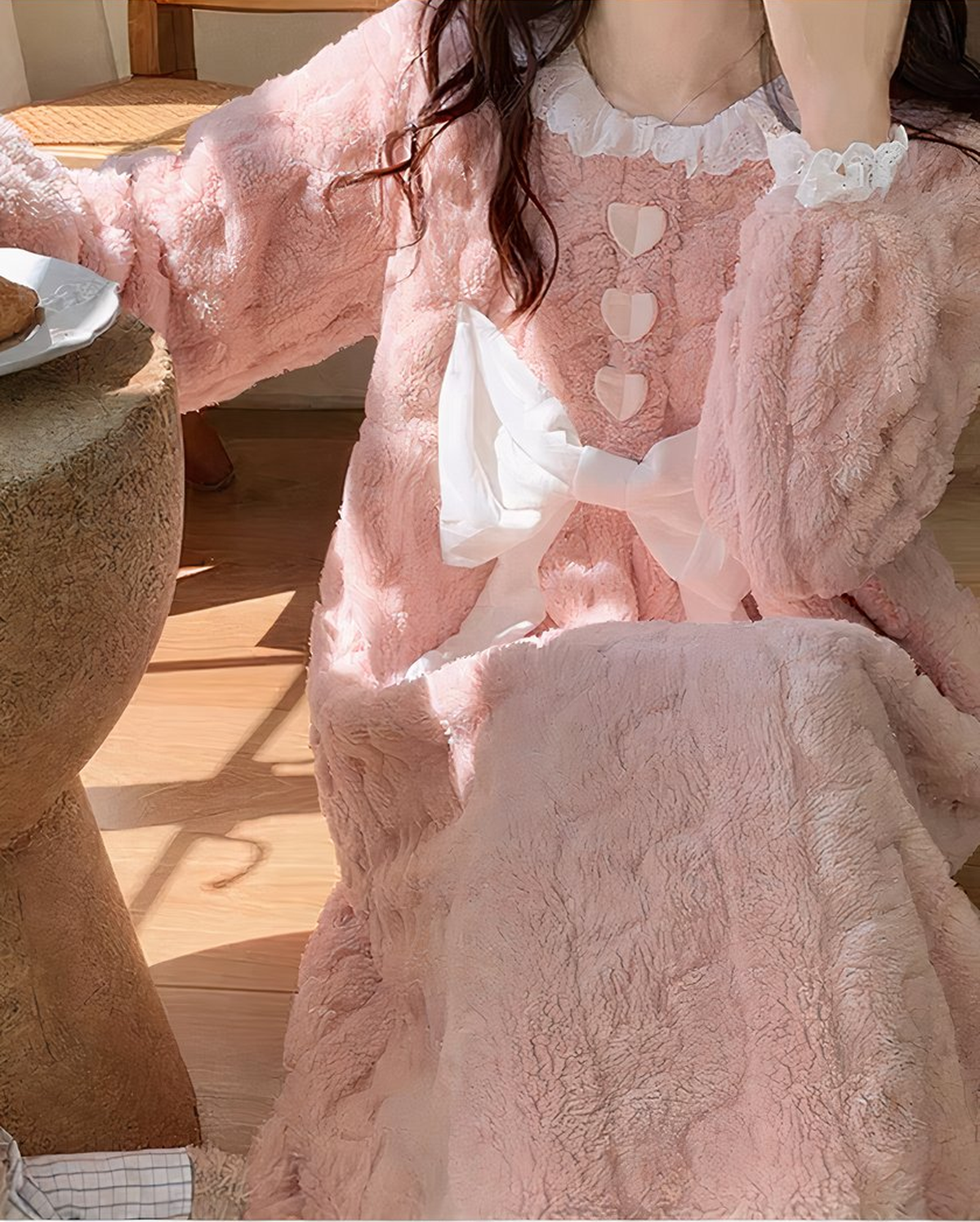 Chemise de nuit rose duveteuse portée assise en pleine lumière : le col de dentelle, les trois cœurs, le nœud et le relief gaufré de l'étoffe