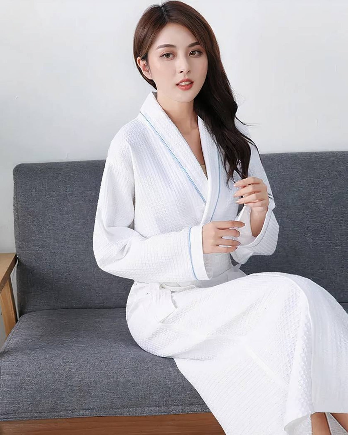 Femme assise portant le peignoir hotel blanc en coton gaufre au lisere bleu, ambiance cosy