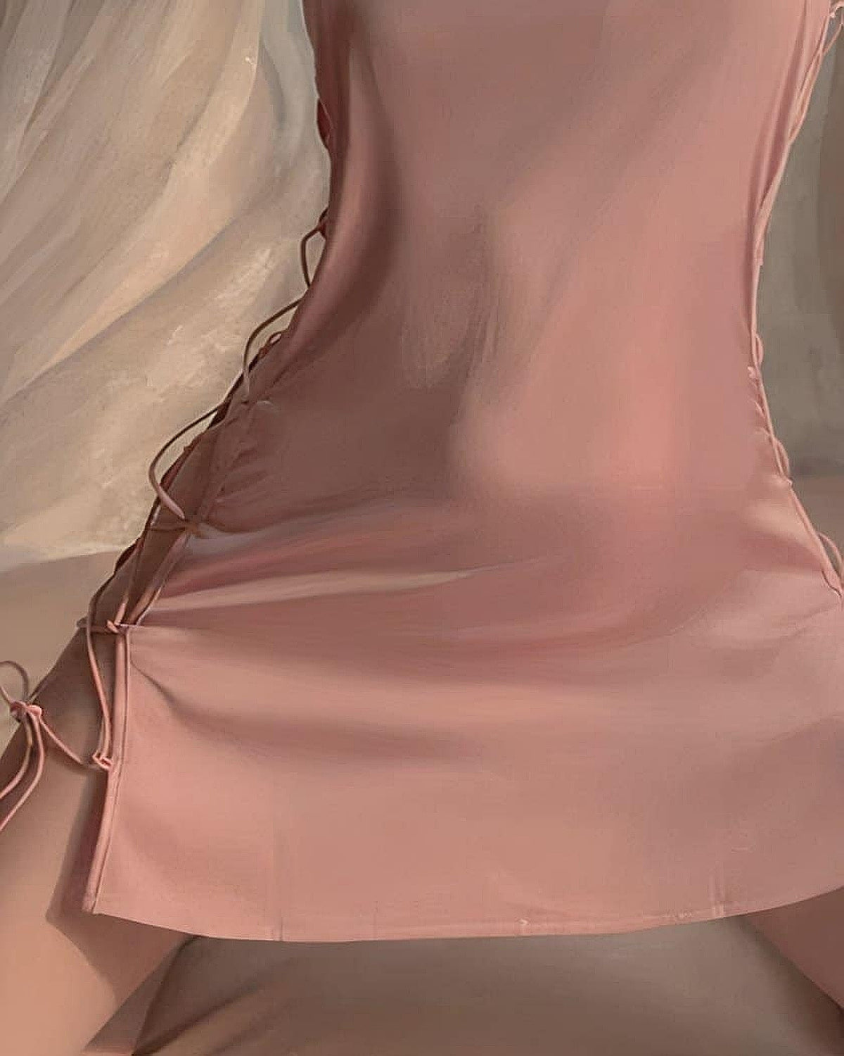 Gros plan sur le laçage latéral et le nœud papillon de la nuisette rose en satin