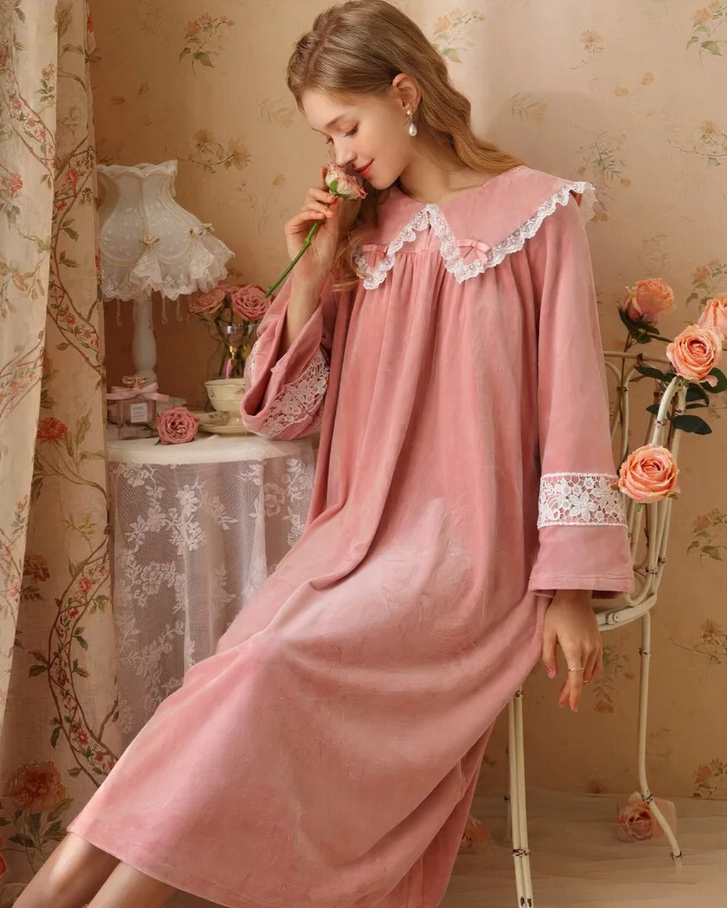 Modele souriante portant la robe de nuit princesse en velours rose, assise tenant une rose, decor vintage