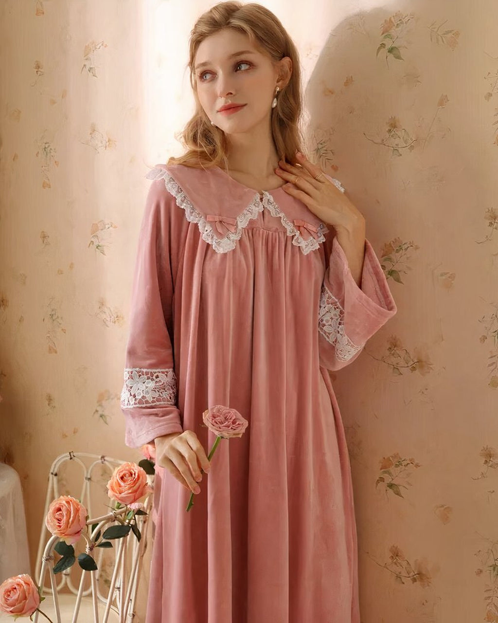 Modele portant la robe de nuit princesse en velours rose, vue de trois-quarts tenant une rose