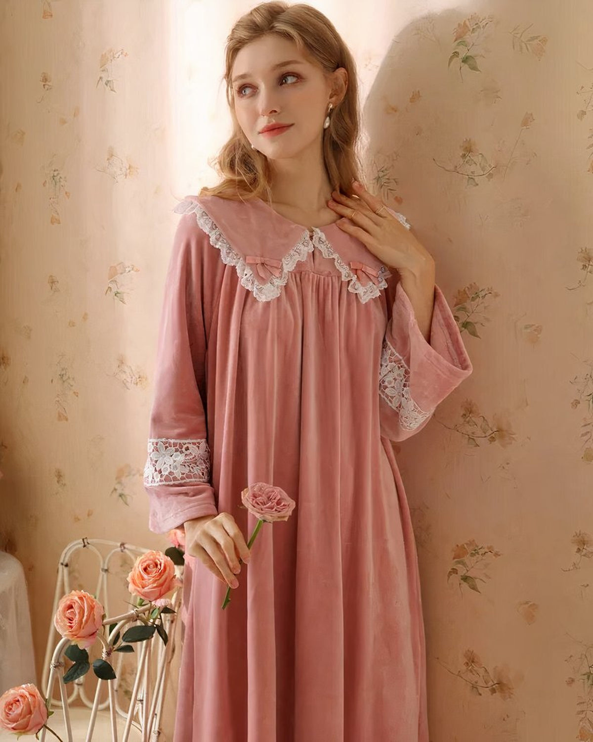 Modele portant la robe de nuit princesse en velours rose, vue de trois-quarts tenant une rose