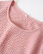 On voit l'encolure ronde d'une chemise de nuit rose poudré en gaze de coton.