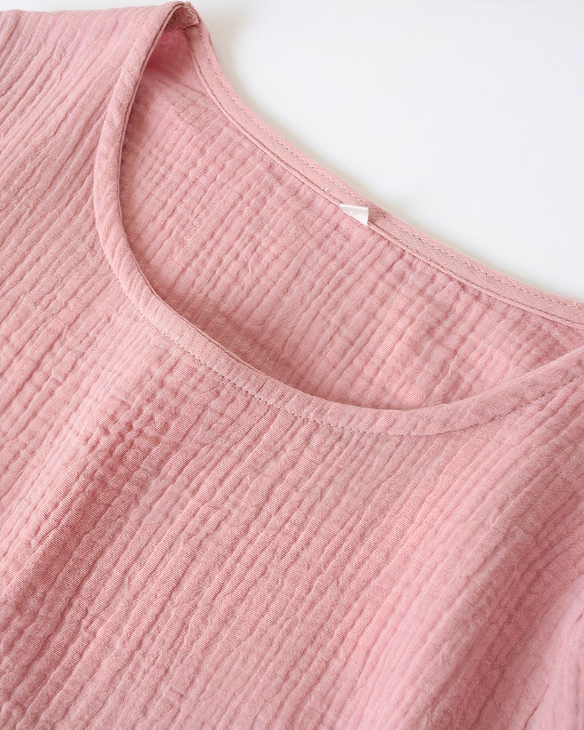 On voit l'encolure ronde d'une chemise de nuit rose poudré en gaze de coton.