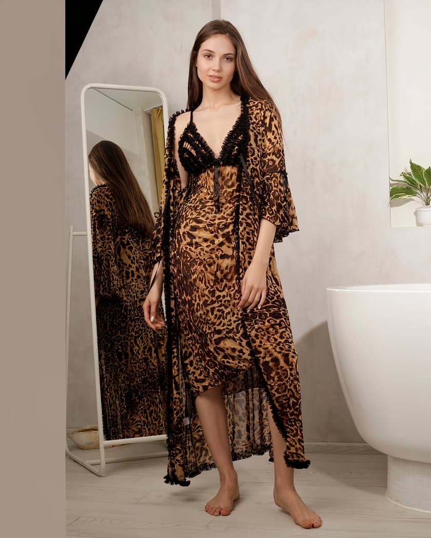 Femme aux cheveux longs châtains à côté d'une baignoire portant une longue nuisette avec bustier à volants noirs imprimé léopard et un kimono assorti par-dessus. Elle est placée de face avec un grand miroir sur pied en arrière-plan.