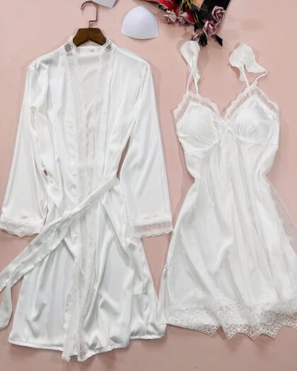 Un kimono blanc satiné avec dentelle transparente sur l'encolure et le bas des manches et avec une ceinture à nouée sur le devant , exposé sur un cintre. A côté, une nuisette assortie blanche satinée avec dentelle, col en v et bretelles en volant. Les deux pièces sont sur un fond rose.