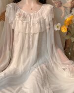 Femme assise sur un chaise portant une nuisette blanche avec des fleurs sur le côté.