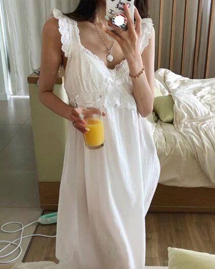 Femme brune portant une nuisette blanche en dentelle dans une chambre un verre de jus d'orange a la main
