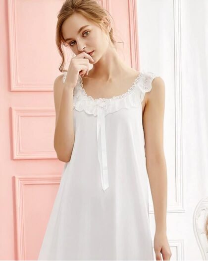 Femme rousse portant une nuisette blanche en dentelles sur le col avec un porte rose derrière et un fauteil en fleur sur le coté droit