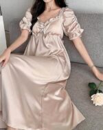 Femme brune assise sur un canapé gris et portant une nuisette élégante en soie et en satin de couleur beige.