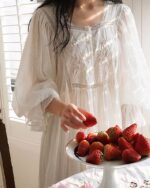 Femme en nuisette blanche mangeant des fraises posées dans une plat blanc sur une table