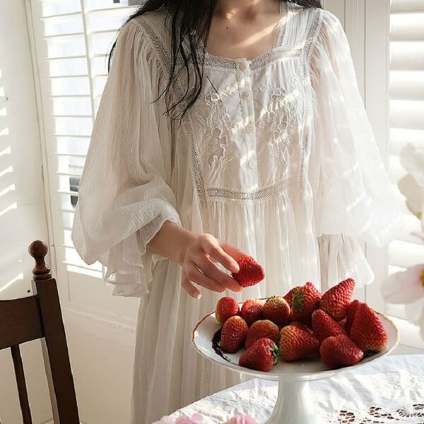 Femme en nuisette blanche mangeant des fraises posées dans une plat blanc sur une table