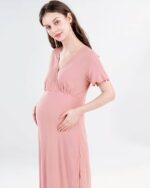 On voit une jeune femme brune à la peau très blanche qui est enceinte. Elle porte une nuisette de maternité manche courte rose poudrée.