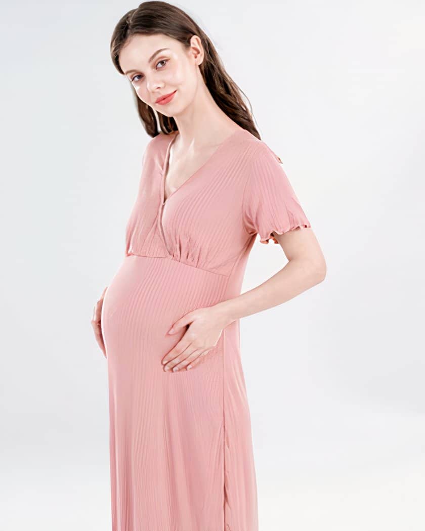 On voit une jeune femme brune à la peau très blanche qui est enceinte. Elle porte une nuisette de maternité manche courte rose poudrée.
