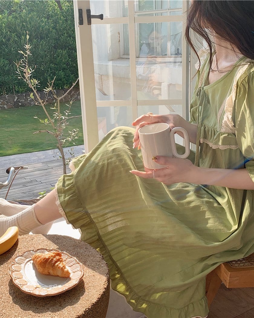Femme portant une nuisette verte vintage. Assise à la fenêtre, avec une tasse à la main, prend son petit déjeuner